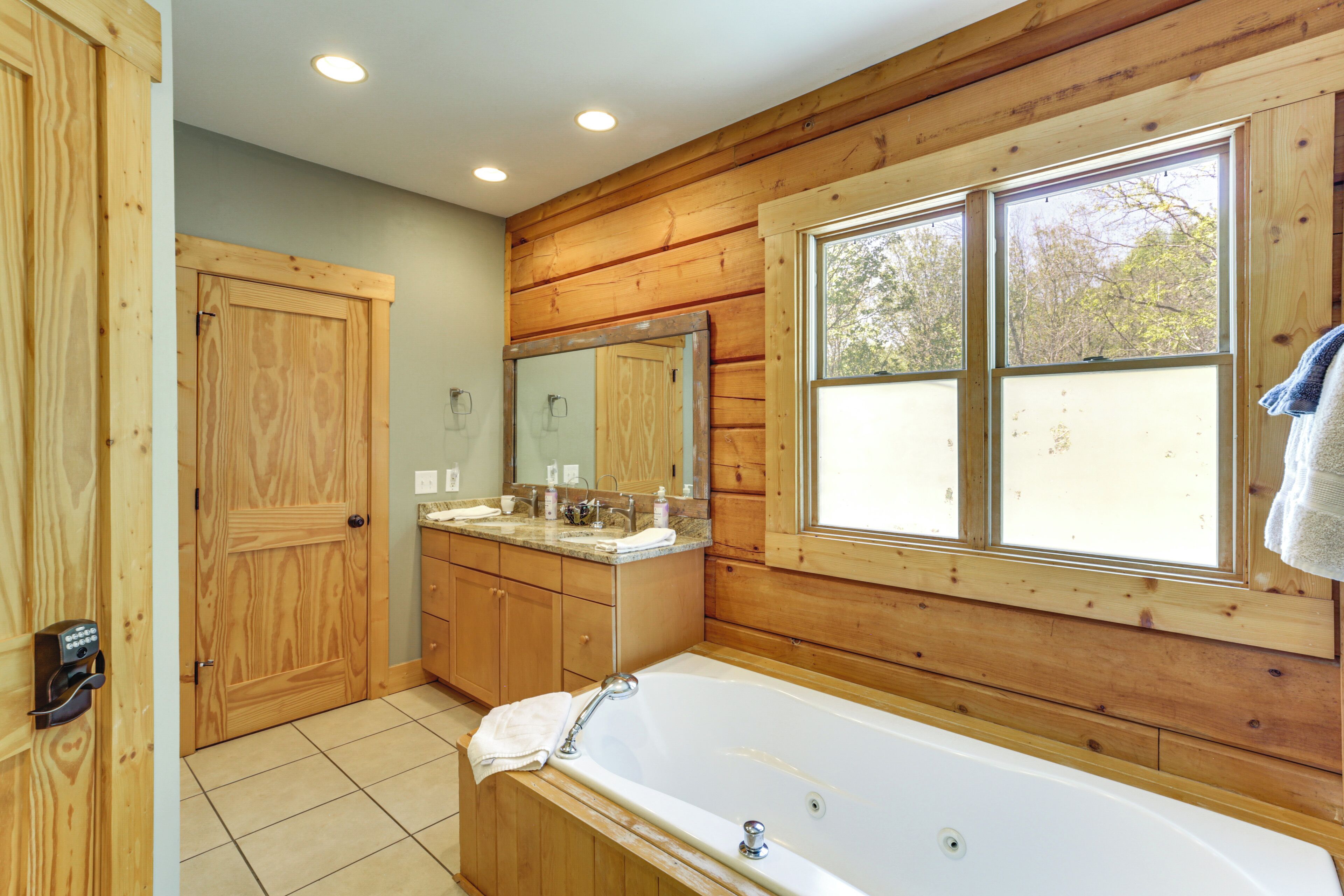 A wooden-paneled bathroom with a large window, a bathtub, and a vanity with a mirror.