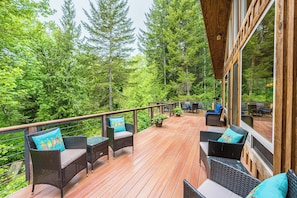 A wooden deck with wicker furniture and a view of a forest. - Olympic Natl Park Base: Luxe Port Angeles Cabin (Port Angeles)