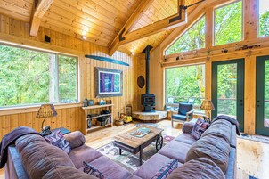 Un interior de madera con sofá, televisor, chimenea y ventanas amplias.