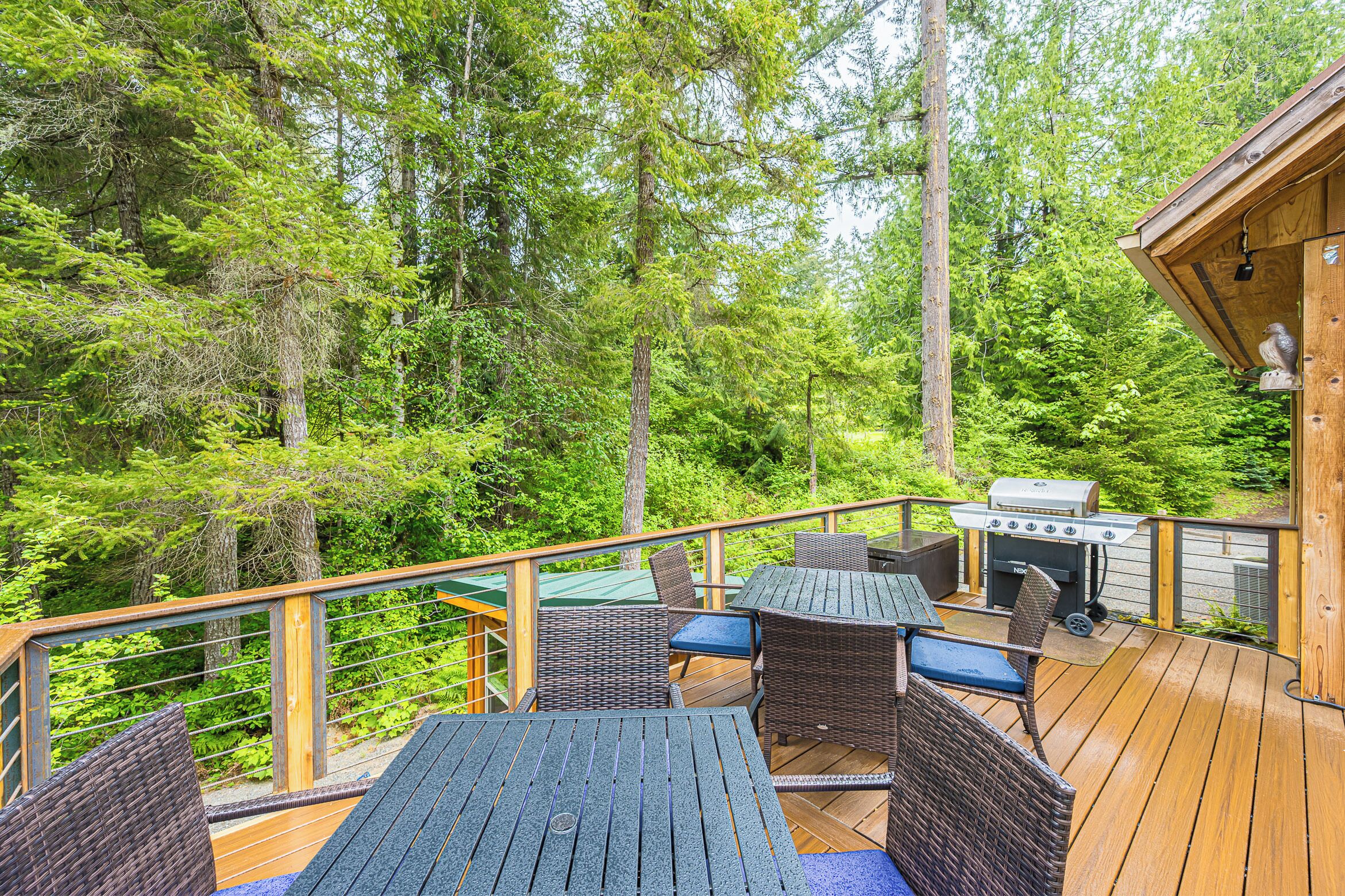 A deck with wicker furniture, a grill, and a view of a forest.