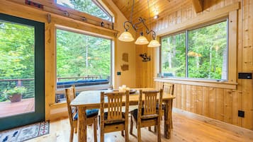A wooden interior with a dining table and chairs, large windows, and a hanging light fixture.
