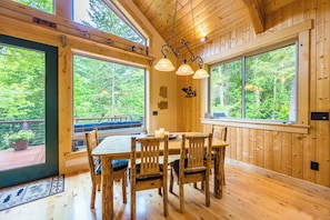 A wooden interior with a dining table and chairs, large windows, and a hanging light fixture. - Olympic Natl Park Base: Luxe Port Angeles Cabin (Port Angeles)