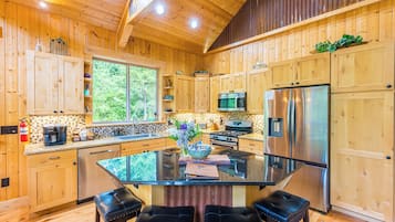 A wooden cabin kitchen with a glass island, stainless steel appliances, and a fire extinguisher.
