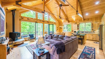 A spacious cabin with a large wooden ceiling, a cozy living area with a sofa and a fireplace, and a kitchen with wooden cabinets.