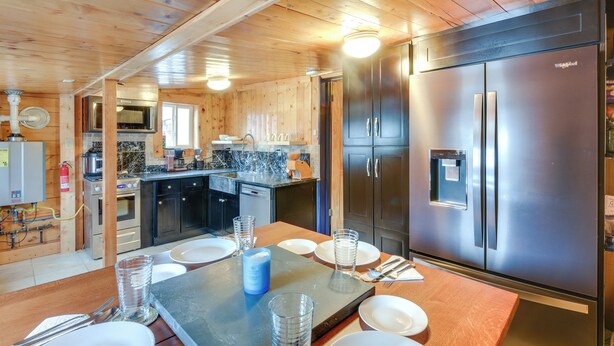 A modern kitchen with wooden walls, stainless steel appliances, and a dining area with a table set for four. - 0601: Downtown Salida Cottage w/ Fireplace + Yard (Salida)