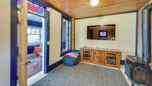 A cozy room with a wooden ceiling, a built-in stove, a television, and a window with a view of the outside. - 0601: Downtown Salida Cottage w/ Fireplace + Yard (Salida)
