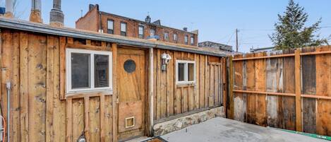 Una construcción de madera con dos ventanas, una puerta, un timbre metálico y un suelo de concreto.