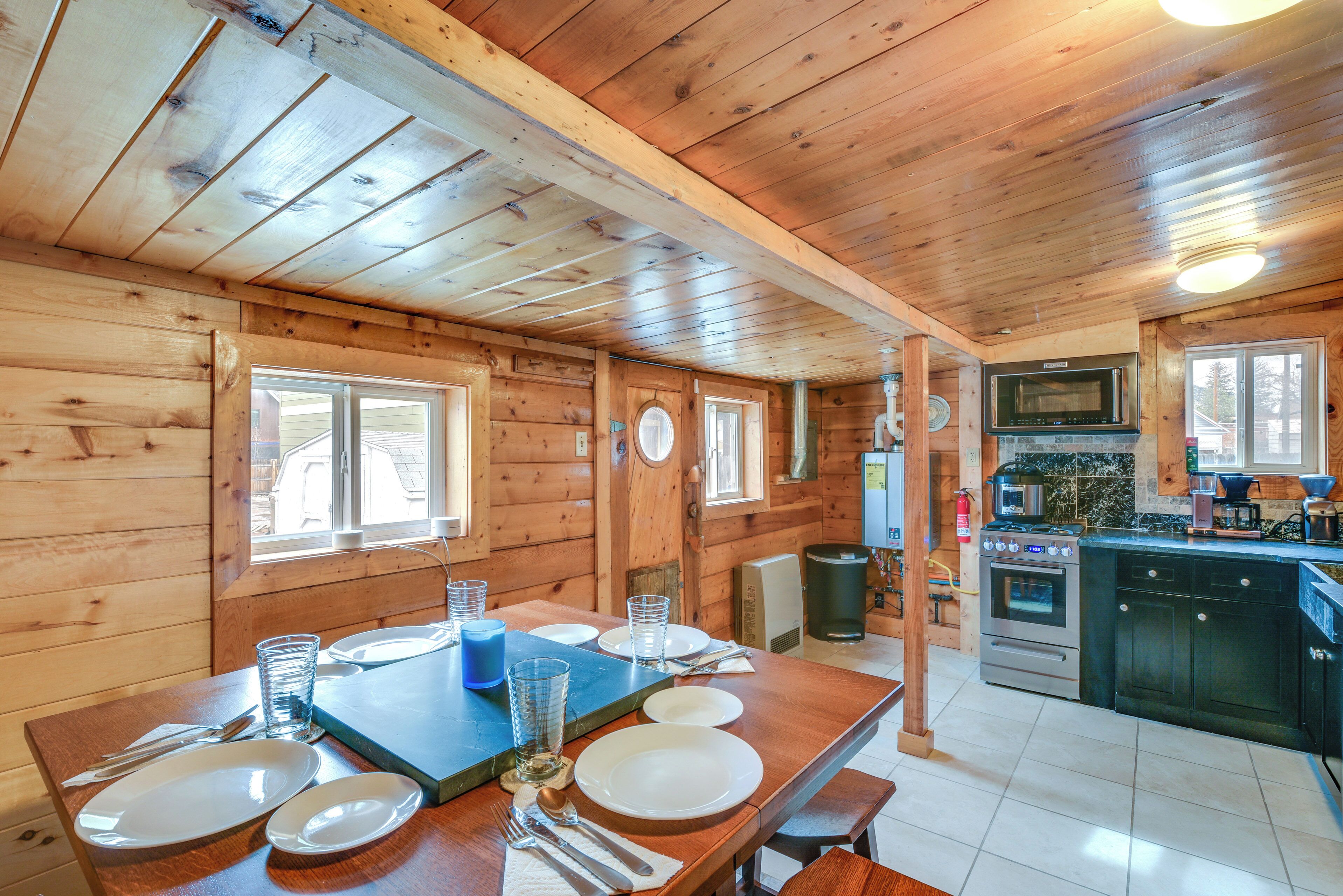 Interior de una cabaña de madera con comedor, cocina y un ventanal grande.