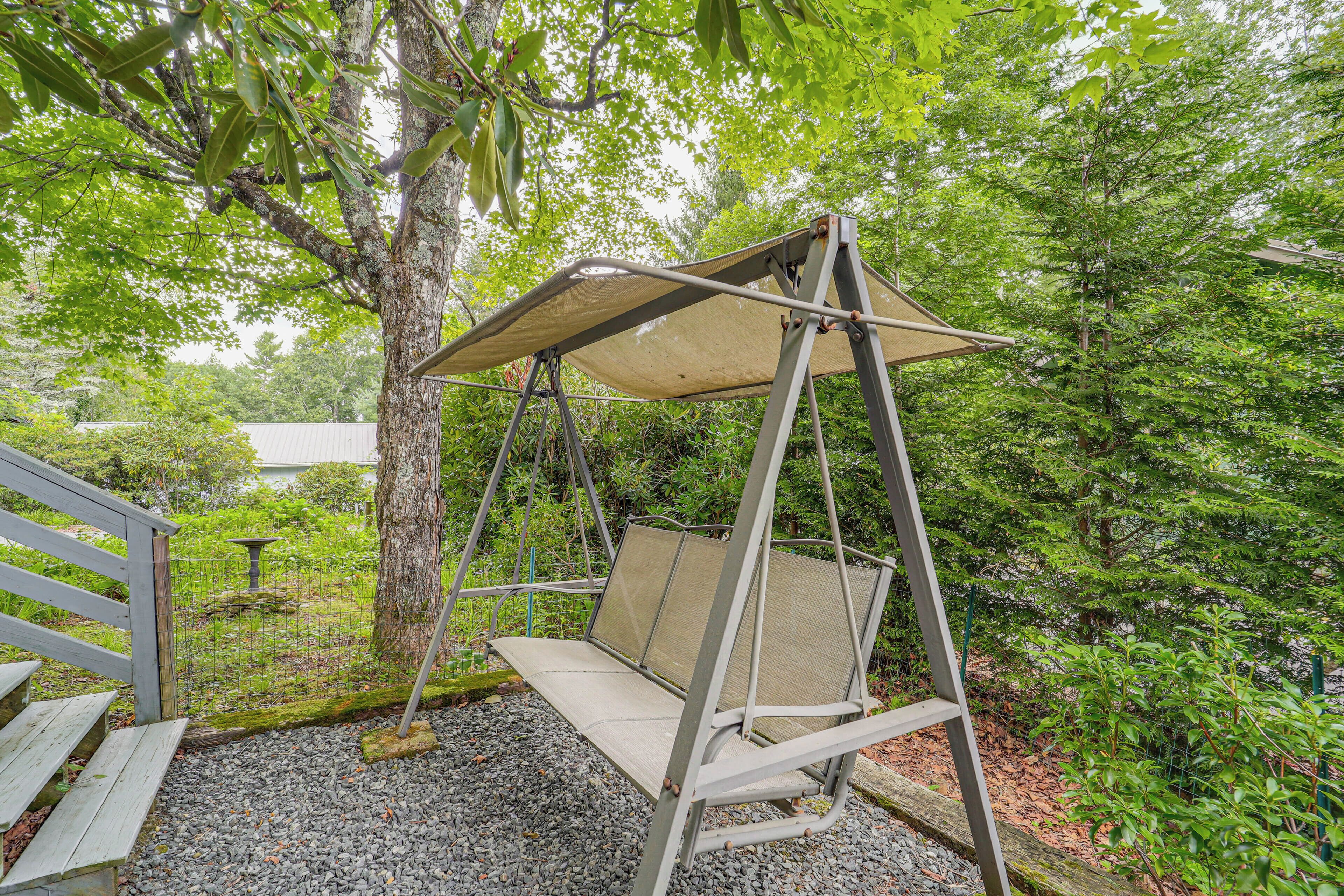 A swing set with a canopy in a garden area with trees and a bench.