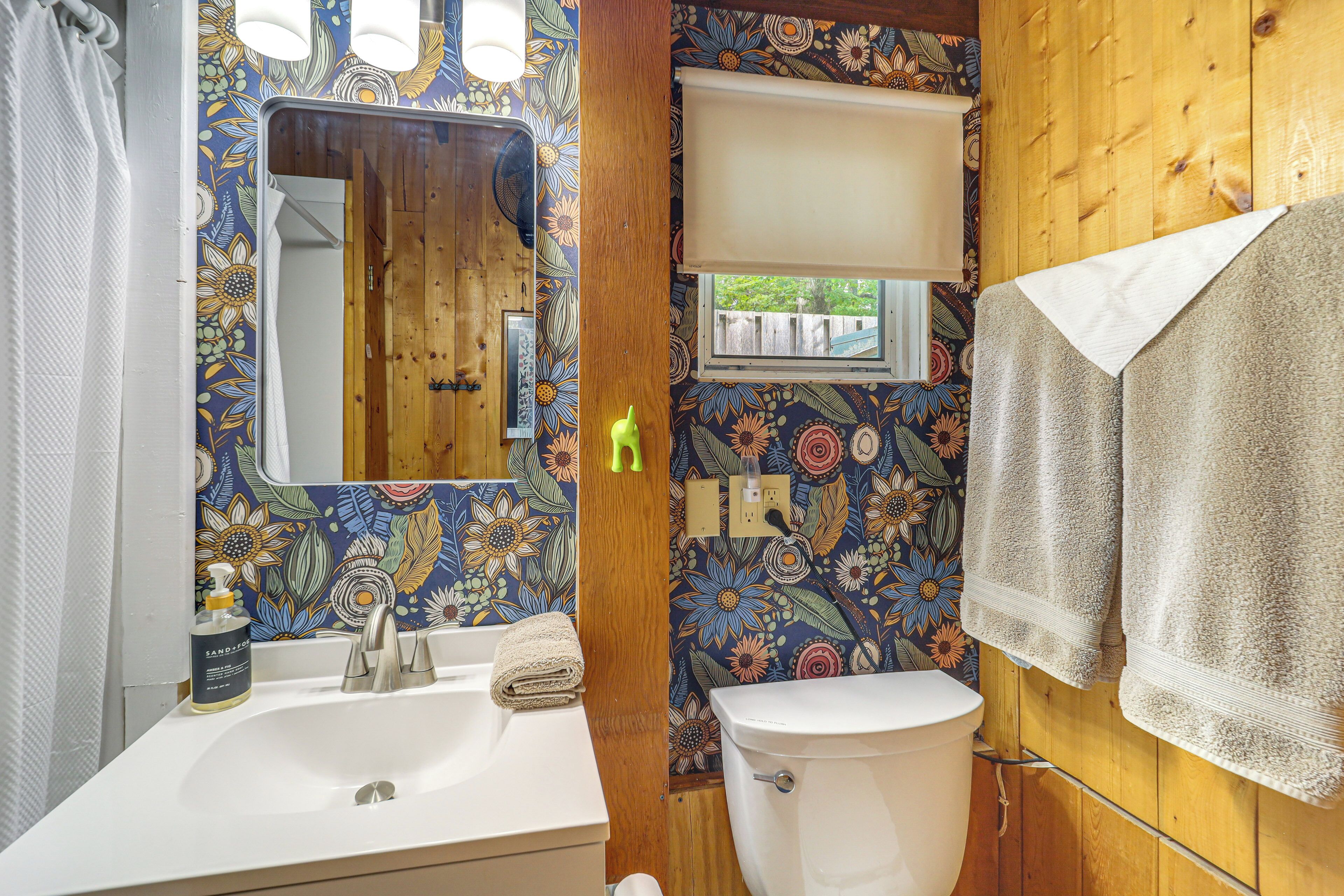 Ein Badezimmer mit Holzvertäfelung, einem weißen Waschbecken, einer Toilette und einem Spiegel mit floralem Wandmuster.