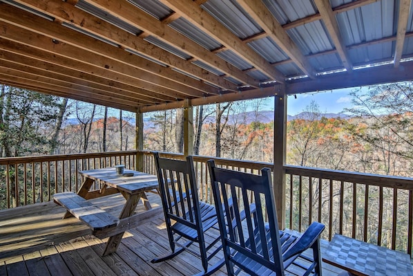 A wooden deck with a table and chairs, overlooking a mountainous landscape.