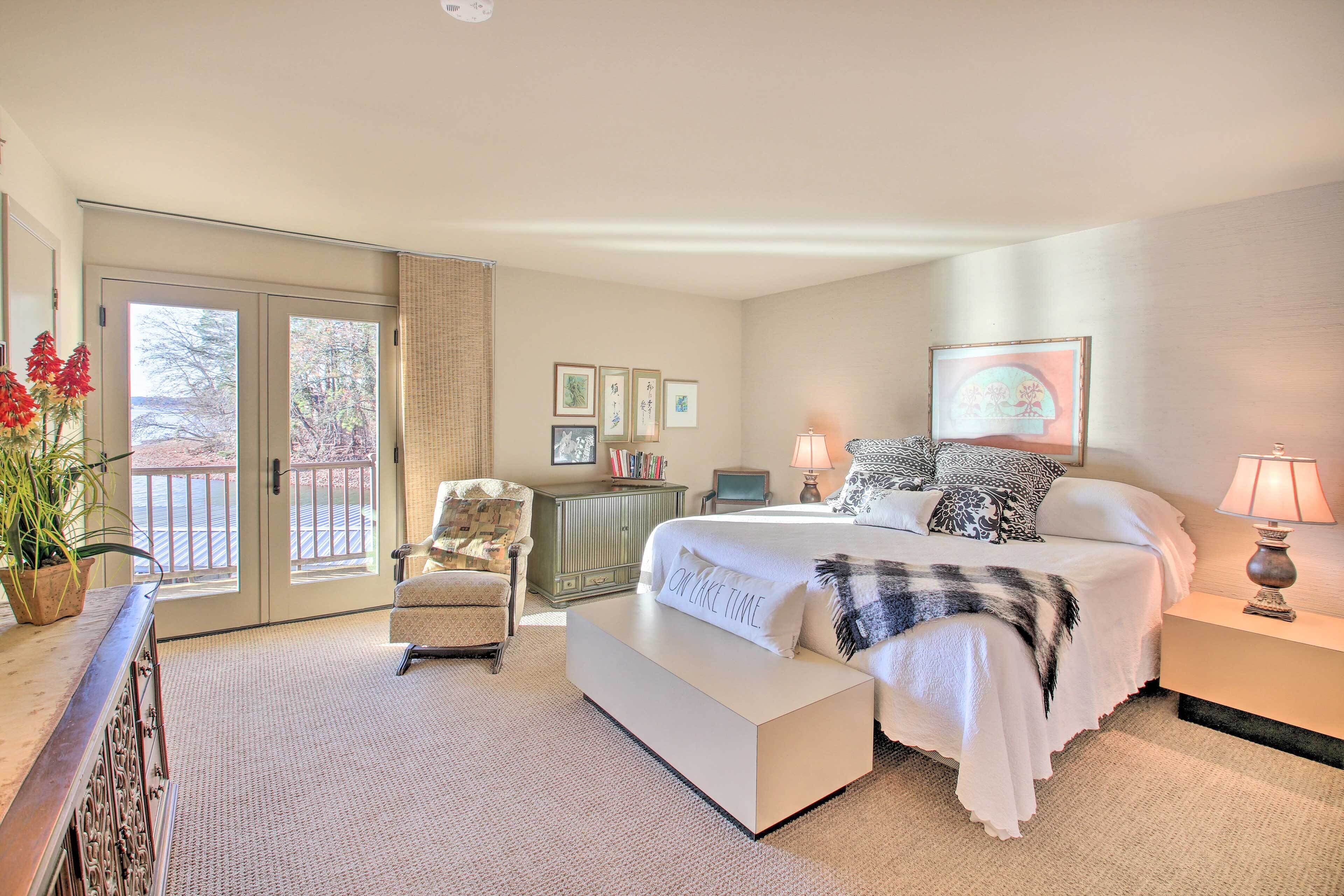 Une chambre avec un grand lit, une chaise, une table de chevet, une lampe et une vue sur l’extérieur, accessible par une porte coulissante.