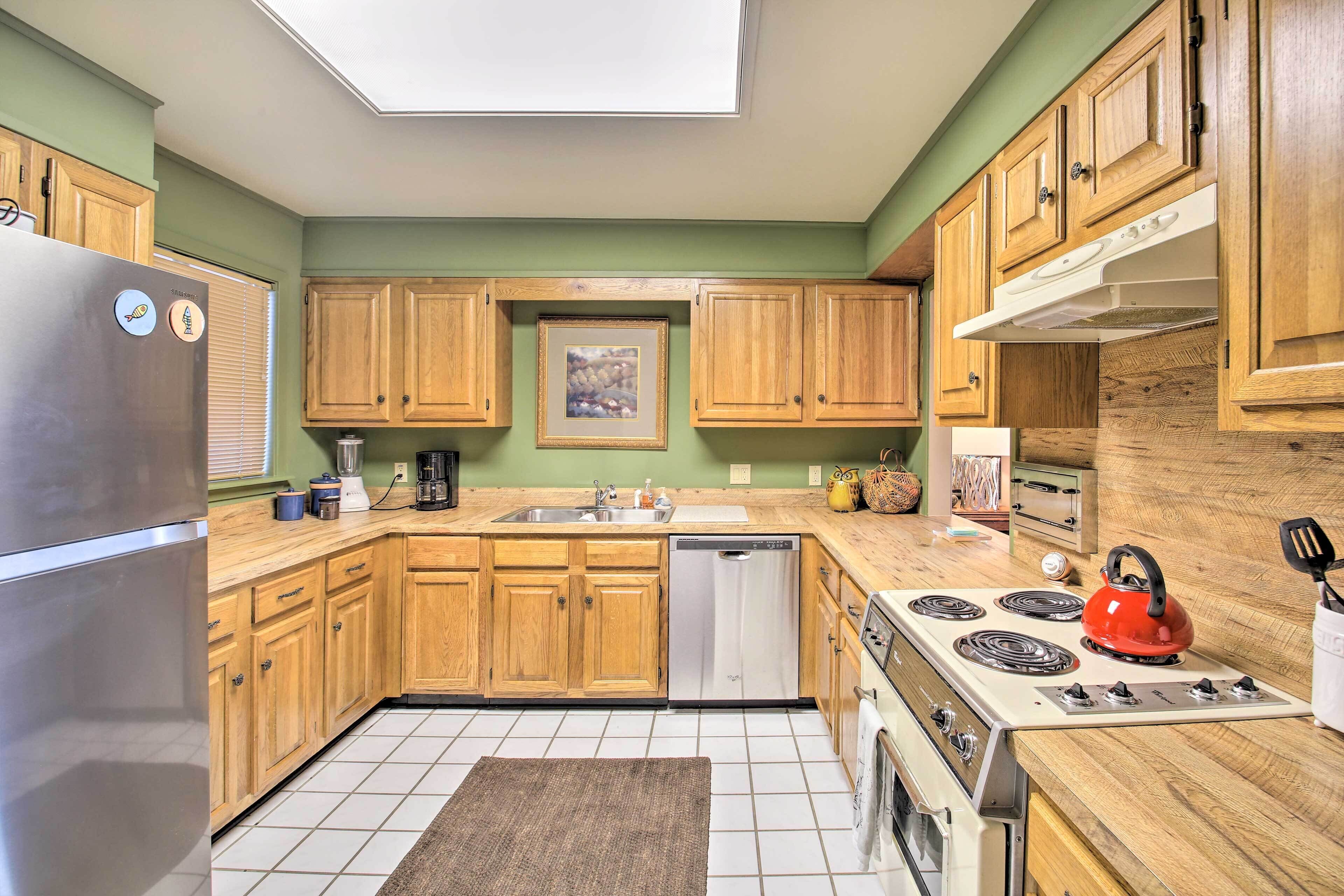 A kitchen with wooden cabinets, a stainless steel refrigerator, a dishwasher, a stove, and a skylight.
