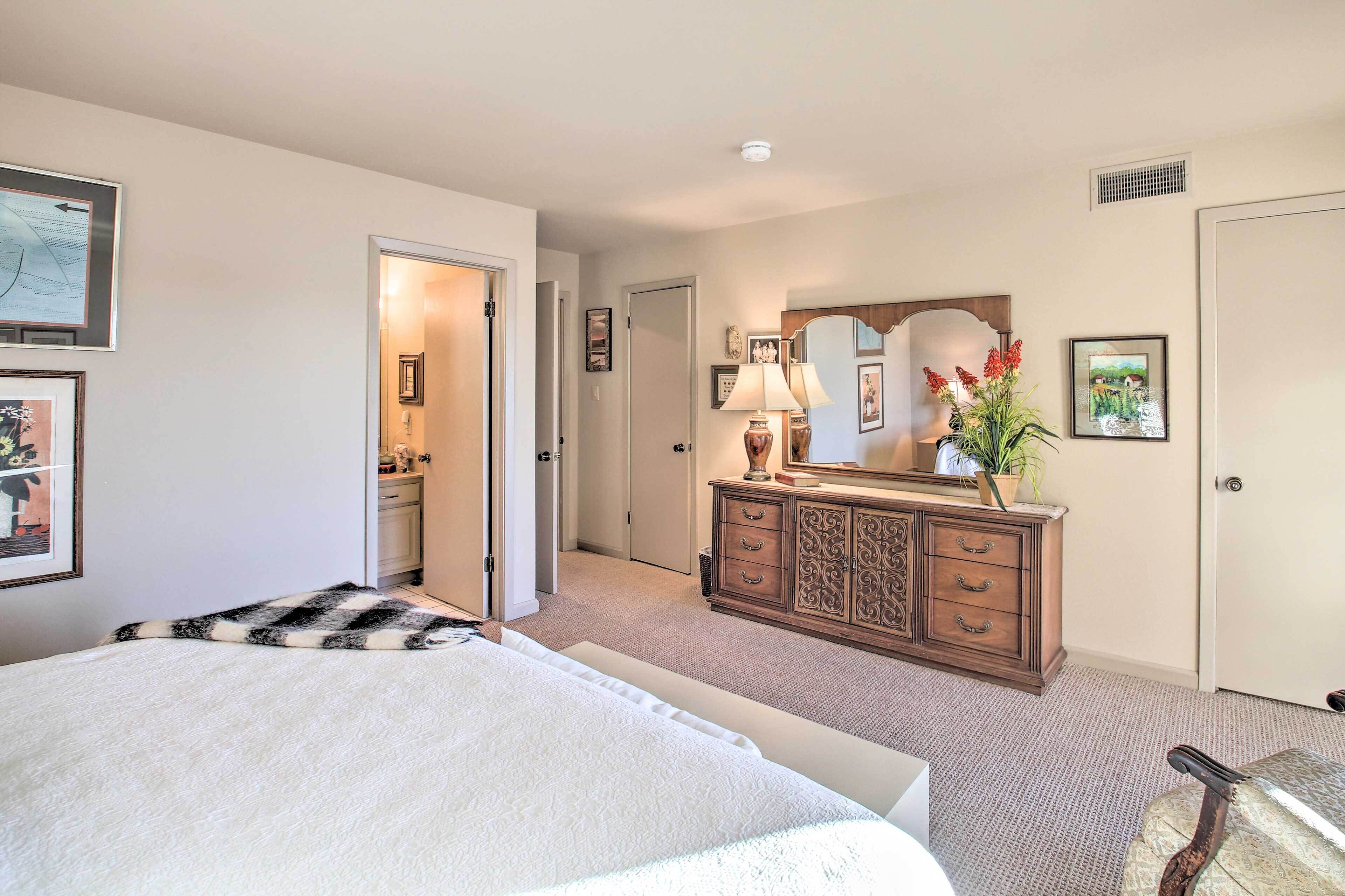 A bedroom with a bed, dresser, mirror, and framed pictures on the walls.
