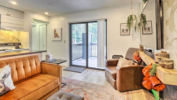 A modern living room with a brown leather sofa, a wooden coffee table, and a fireplace. There is a sliding glass door leading to a balcony with a view of trees. - Cozy Breckenridge Condo: Free Ski Shuttle Access! (Breckenridge)
