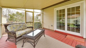 A covered porch with a wicker sofa and a glass-top table, a red wooden deck, and a sliding glass door leading to a backyard. - Cozy Home w/ Fenced Yard < 1 Mi Downtown Matthews! (Matthews)