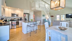 A spacious kitchen with modern appliances, a dining area with a white table, and a staircase leading to an upper level. - Carefree Coastal Getaway - Walk to Long Beach (Oak Island)