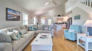 A spacious living room with a sectional sofa, a coffee table, and a blue armchair. A kitchen is visible in the background with a dining area. - Carefree Coastal Getaway - Walk to Long Beach (Oak Island)