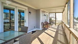 A covered outdoor area with a glass table and wicker chairs, wooden deck, and a view of neighboring houses. - Carefree Coastal Getaway - Walk to Long Beach (Oak Island)