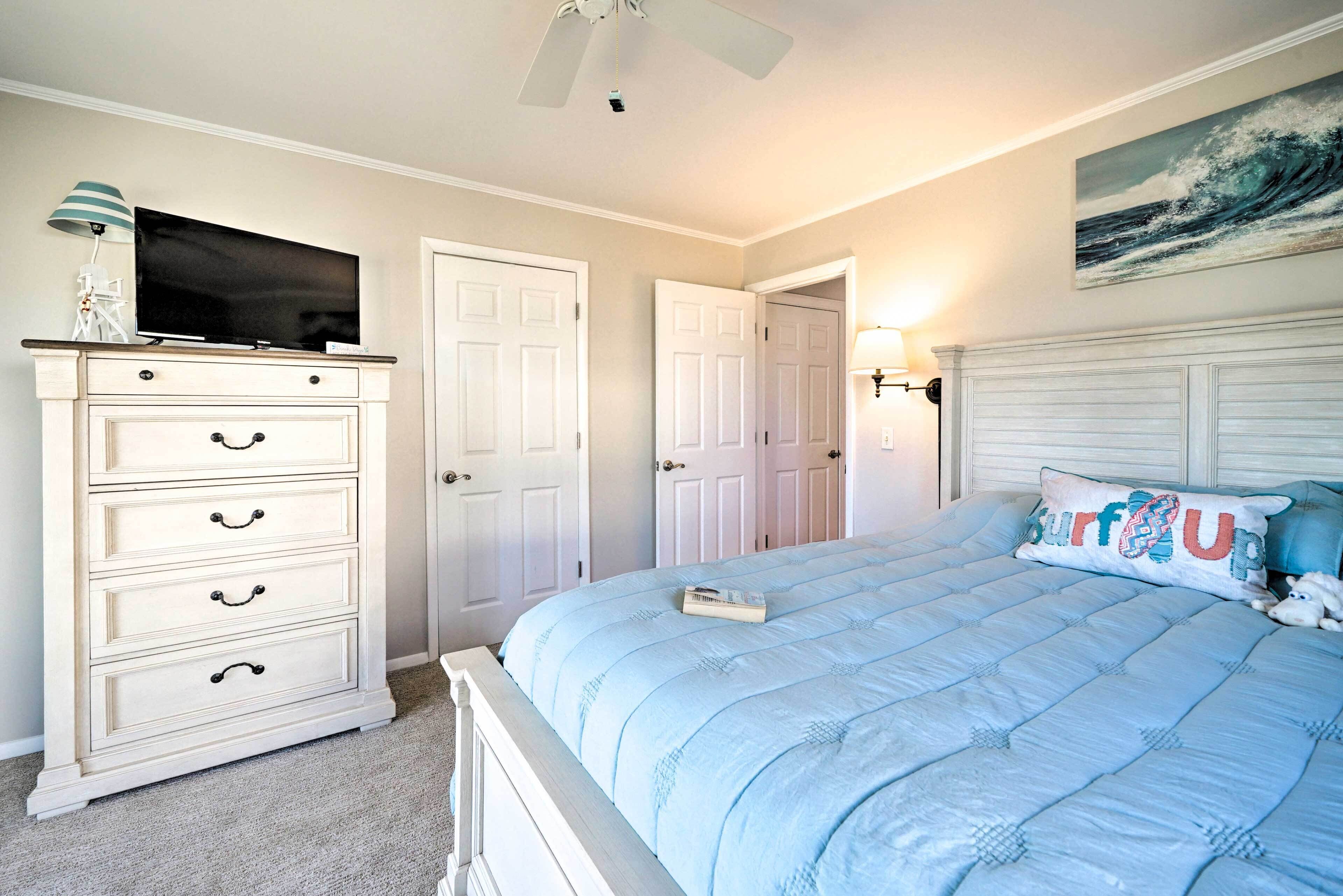 A bedroom with a bed, dresser, television, and a painting on the wall.