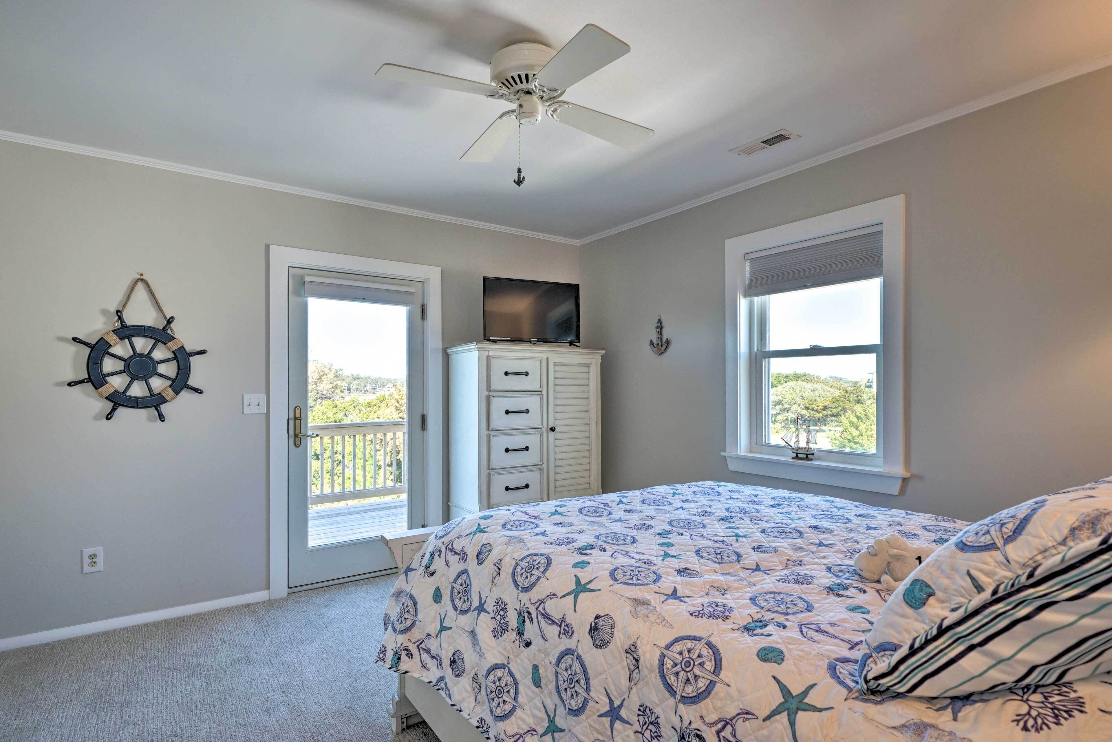 Une chambre à coucher avec un lit, un ventilateur de plafond, un téléviseur posé sur un meuble et une vue à travers la porte.