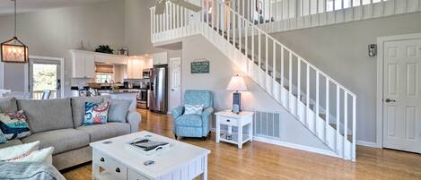 A spacious living area with a white staircase, a kitchen in the background, and a ceiling fan.