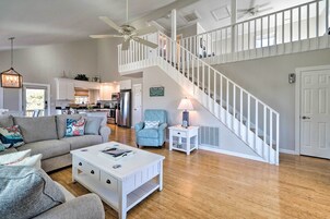 A spacious living area with a white staircase, a kitchen in the background, and a ceiling fan.