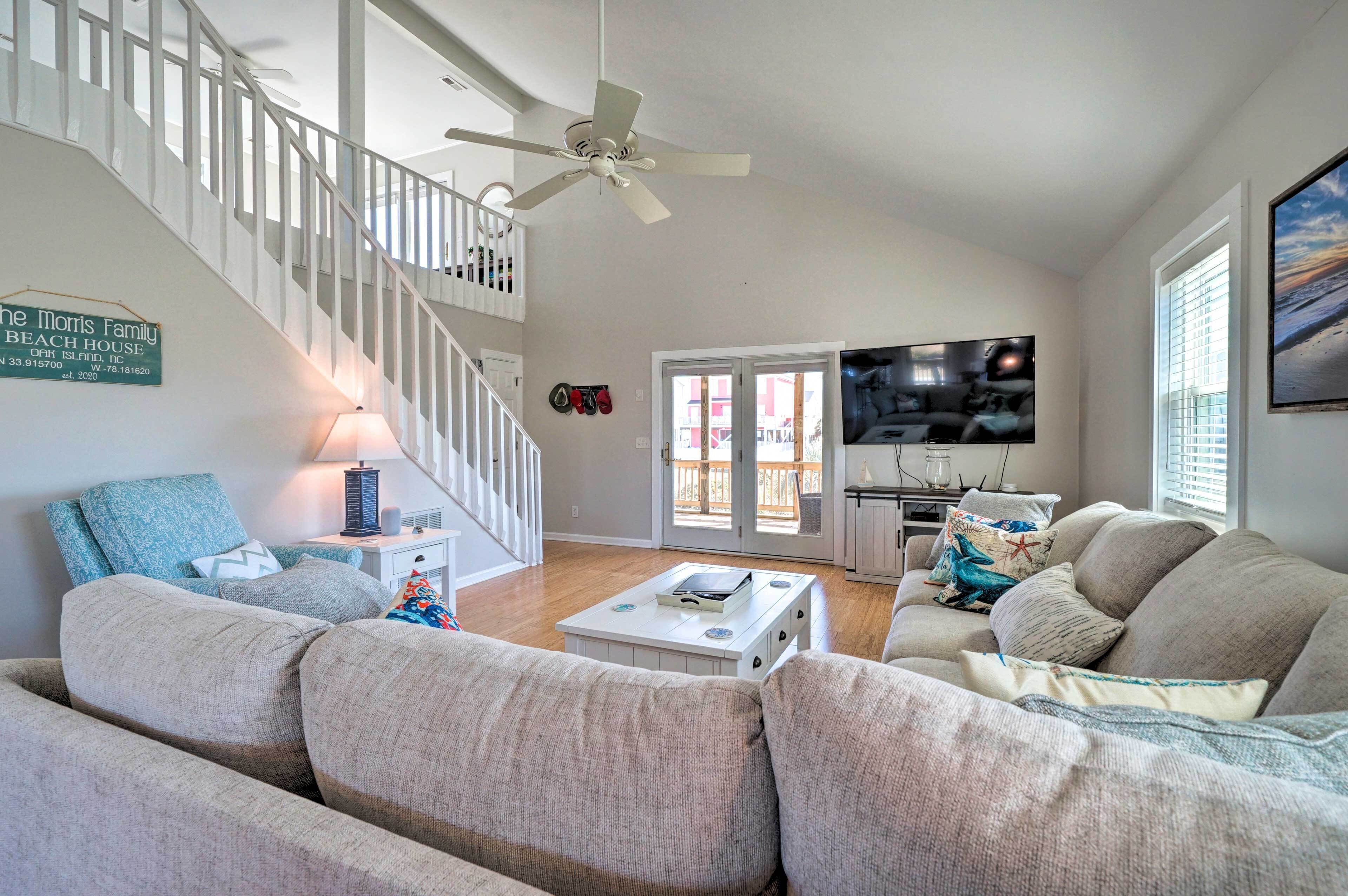 Un salon avec un escalier, un ventilateur de plafond, un téléviseur à écran plat et un coin repas comprenant une table et des chaises.