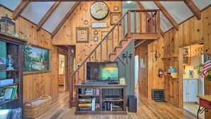 A wooden interior with a staircase, a television on a wooden stand, and a bookshelf. - Lakeview Lodge Fit for Groups < 1 Mile to Lake! (Cedar Glen)