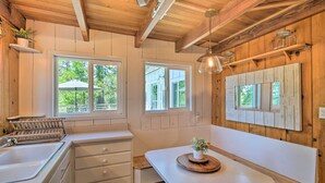 A kitchen with wooden beams, white cabinets, a sink, and a window overlooking greenery. - Lakeview Lodge Fit for Groups < 1 Mile to Lake! (Cedar Glen)