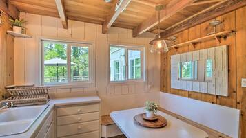 A kitchen with wooden beams, white cabinets, a sink, and a window overlooking greenery.
