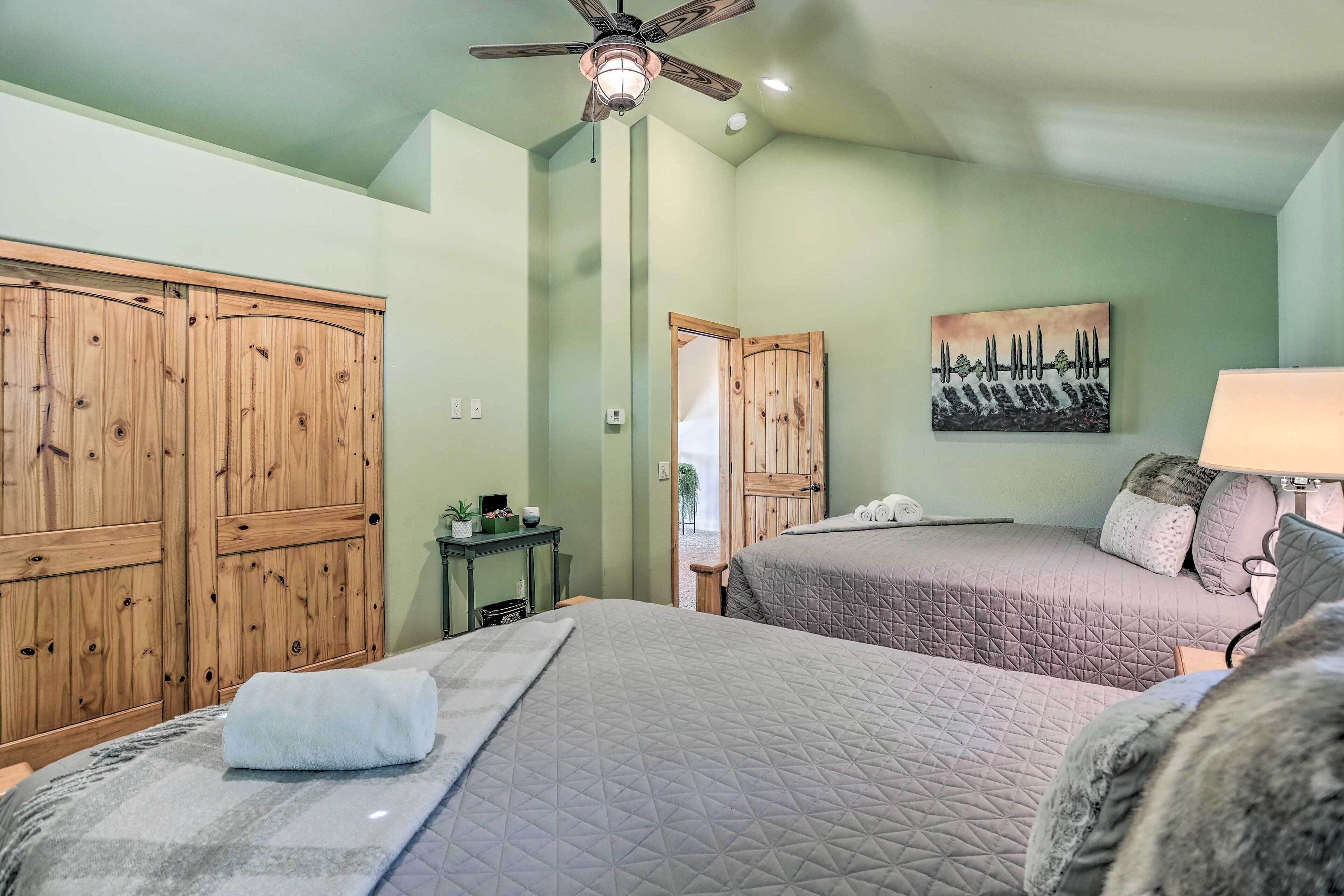 A bedroom with two beds, a ceiling fan, a painting, and a wooden wardrobe.