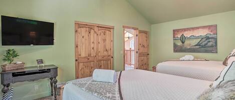 Een slaapkamer met twee bedden, een bureau met een flatscreen televisie, houten kasten en een schilderij aan de muur.