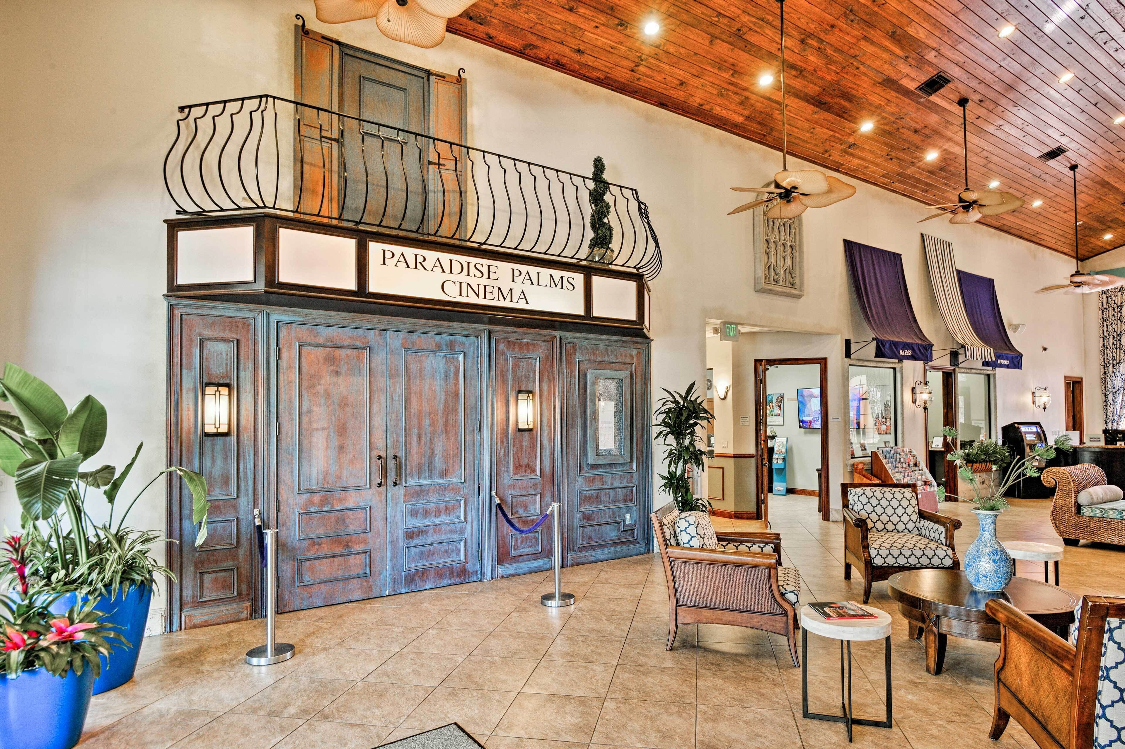 A lobby with a wooden ceiling, a balcony with a sign reading "Paradise Palms Cinema," and a seating area with various chairs and tables.
