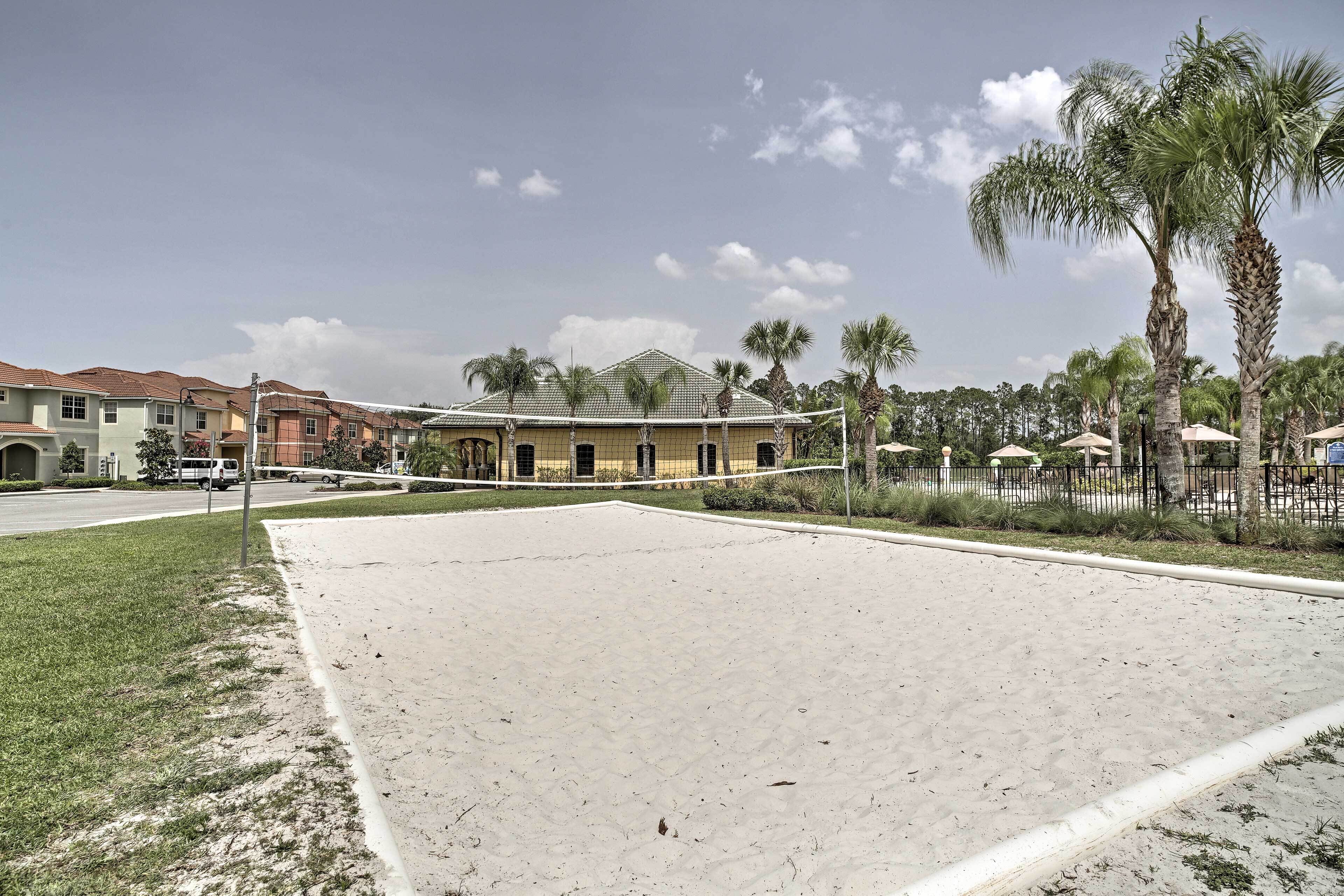 A sandy volleyball court with a net, surrounded by palm trees and a building with a tiled roof.