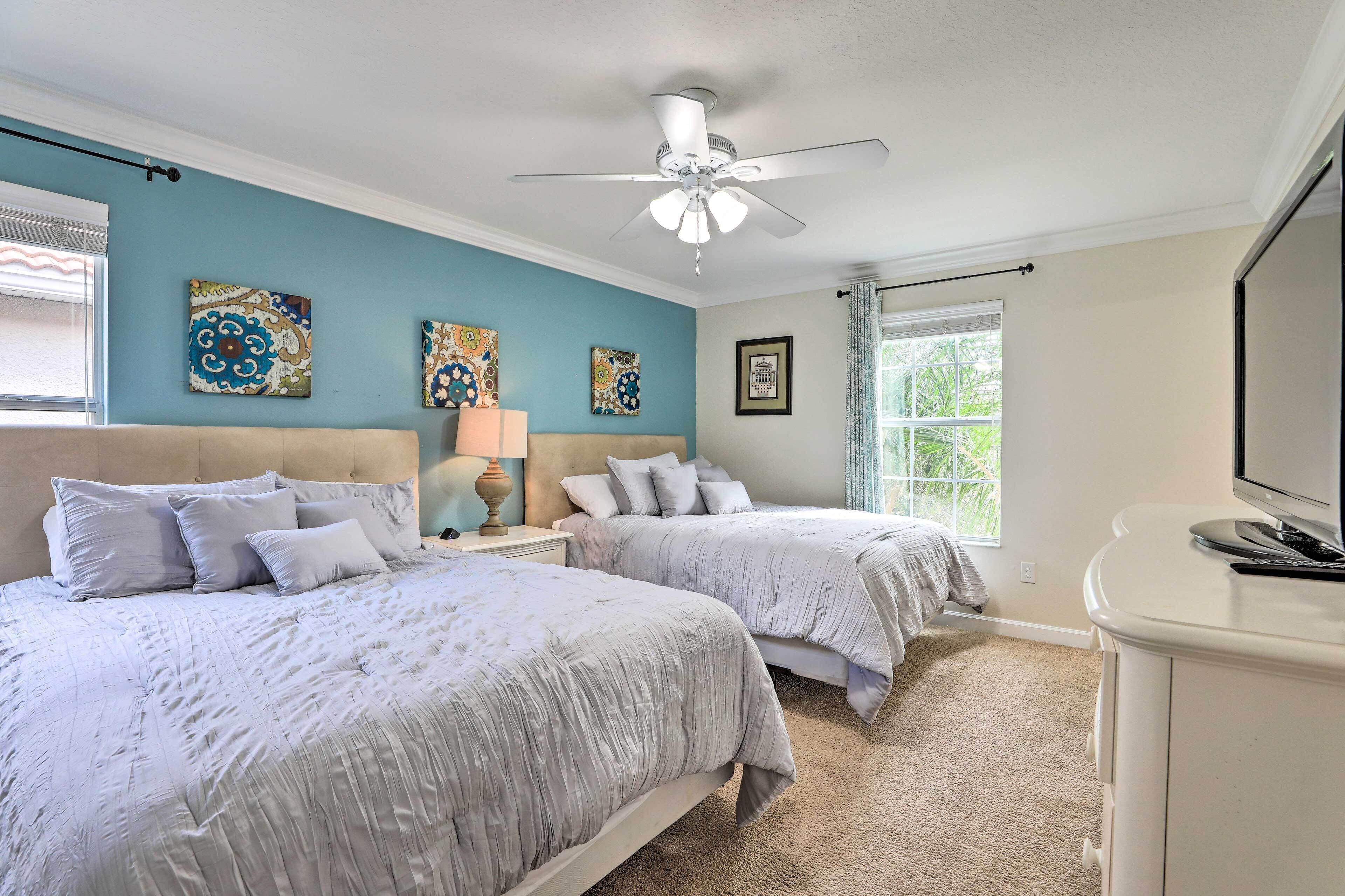 A bedroom with two beds, a ceiling fan, artwork on the walls, a lamp, and a TV.