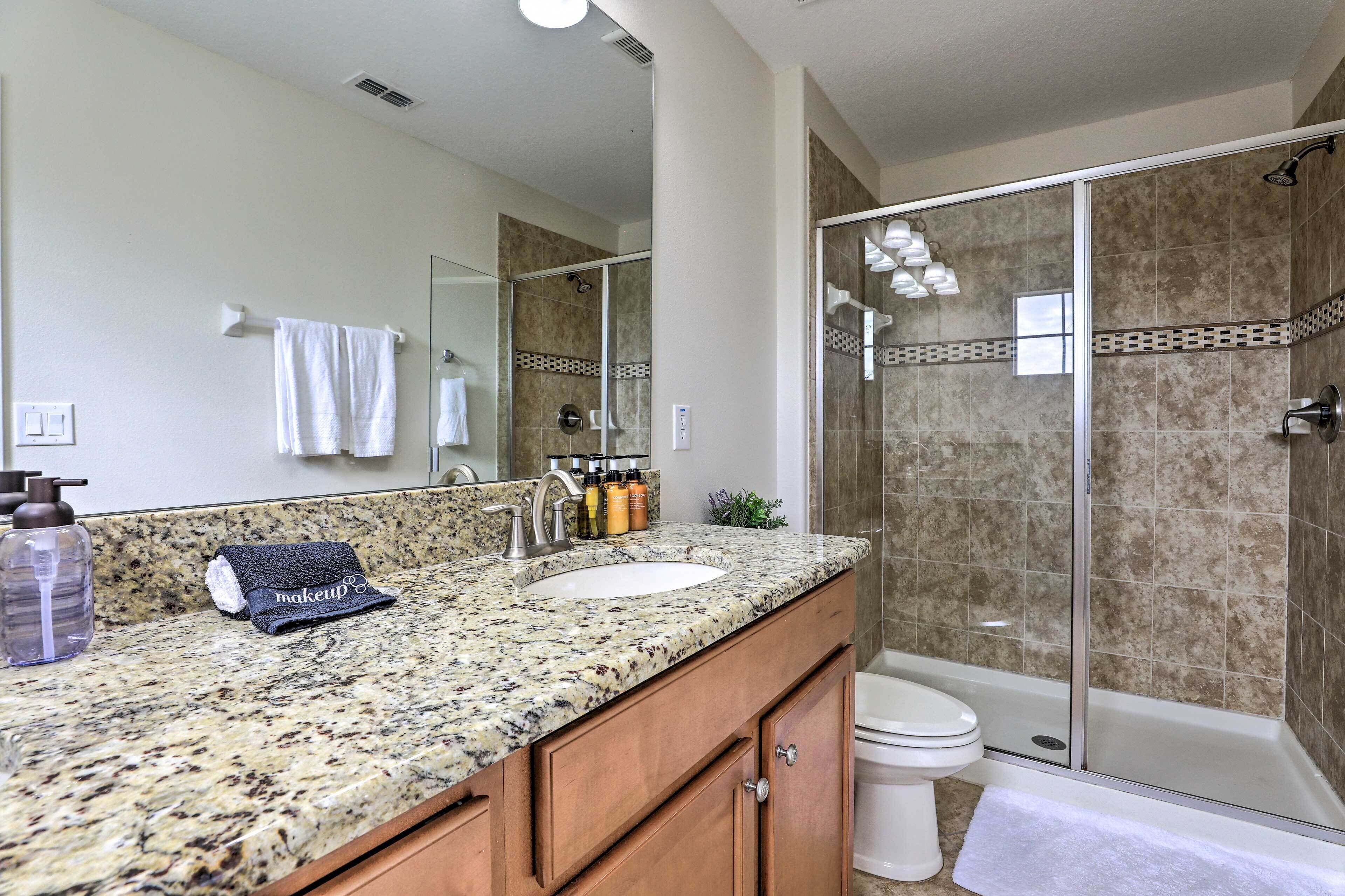 A bathroom with a granite countertop, a sink, a mirror, a towel rack, and a shower area.