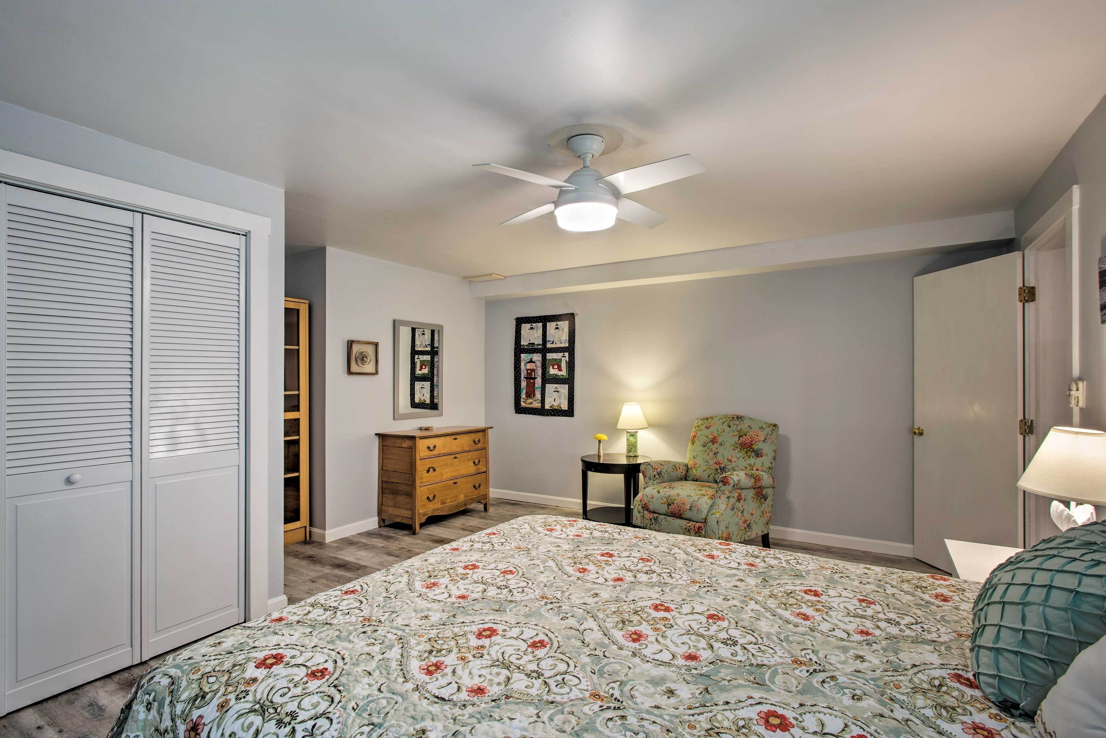 Une chambre à coucher comprenant un lit, une chaise, une commode, un ventilateur de plafond et une armoire.