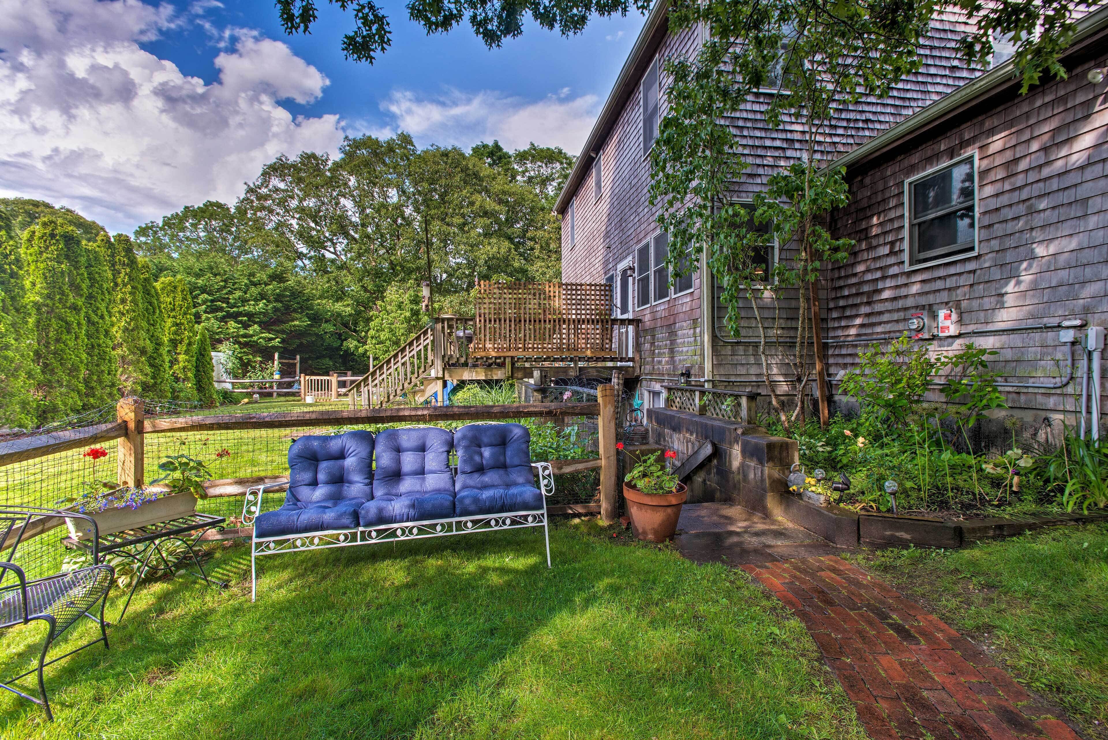 A backyard with a blue sofa, a wooden deck, and a house with a brick pathway.