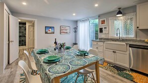 A modern kitchen with white cabinets, a stainless steel dishwasher, and a dining area with a patterned tablecloth and green plates. - Martha's Vineyard Apt ~ 1 Mile to Inkwell Beach! (Oak Bluffs)
