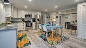 A modern kitchen with white cabinets, stainless steel appliances, and a dining area with a table set for four. - Martha's Vineyard Apt ~ 1 Mile to Inkwell Beach! (Oak Bluffs)