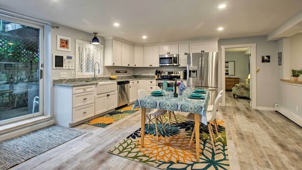 A modern kitchen with white cabinets, stainless steel appliances, and a dining area with a patterned tablecloth. - Martha's Vineyard Apt ~ 1 Mile to Inkwell Beach! (Oak Bluffs)