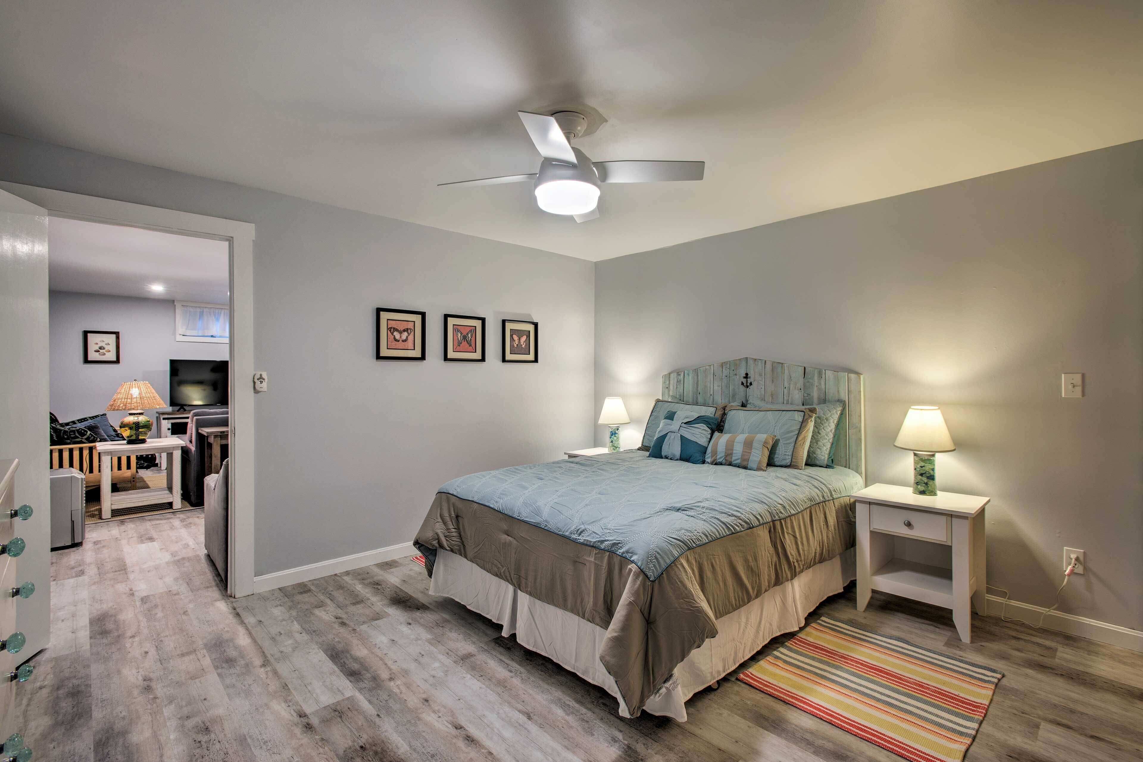 Quarto com cama, luminárias de cabeceira, ventilador de teto e tapete listrado.