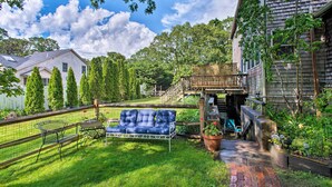 A backyard with a blue outdoor sofa, a wooden deck, and a brick pathway. - Martha's Vineyard Apt ~ 1 Mile to Inkwell Beach! (Oak Bluffs)