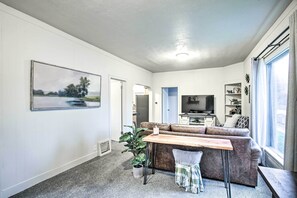 A modern living room with a grey sofa, a wooden coffee table, and a large window with curtains. - High-end & Homey Family Abode: Walk Downtown! (Coeur d'Alene)