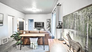 A modern living room with a sofa, a wooden coffee table, a television, and a large painting of a forest scene. - High-end & Homey Family Abode: Walk Downtown! (Coeur d'Alene)