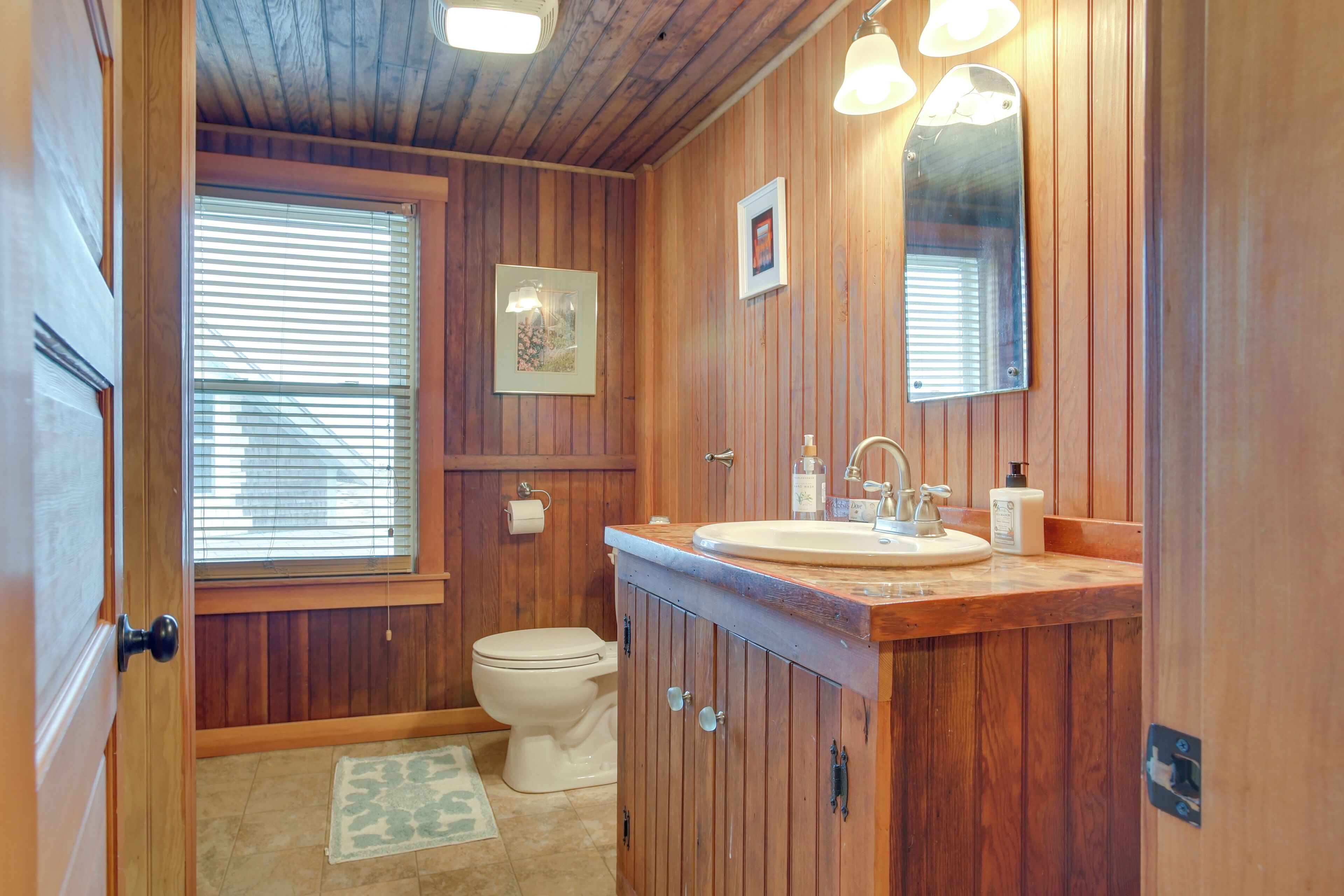 A wooden-paneled bathroom with a toilet, sink, and mirrors.