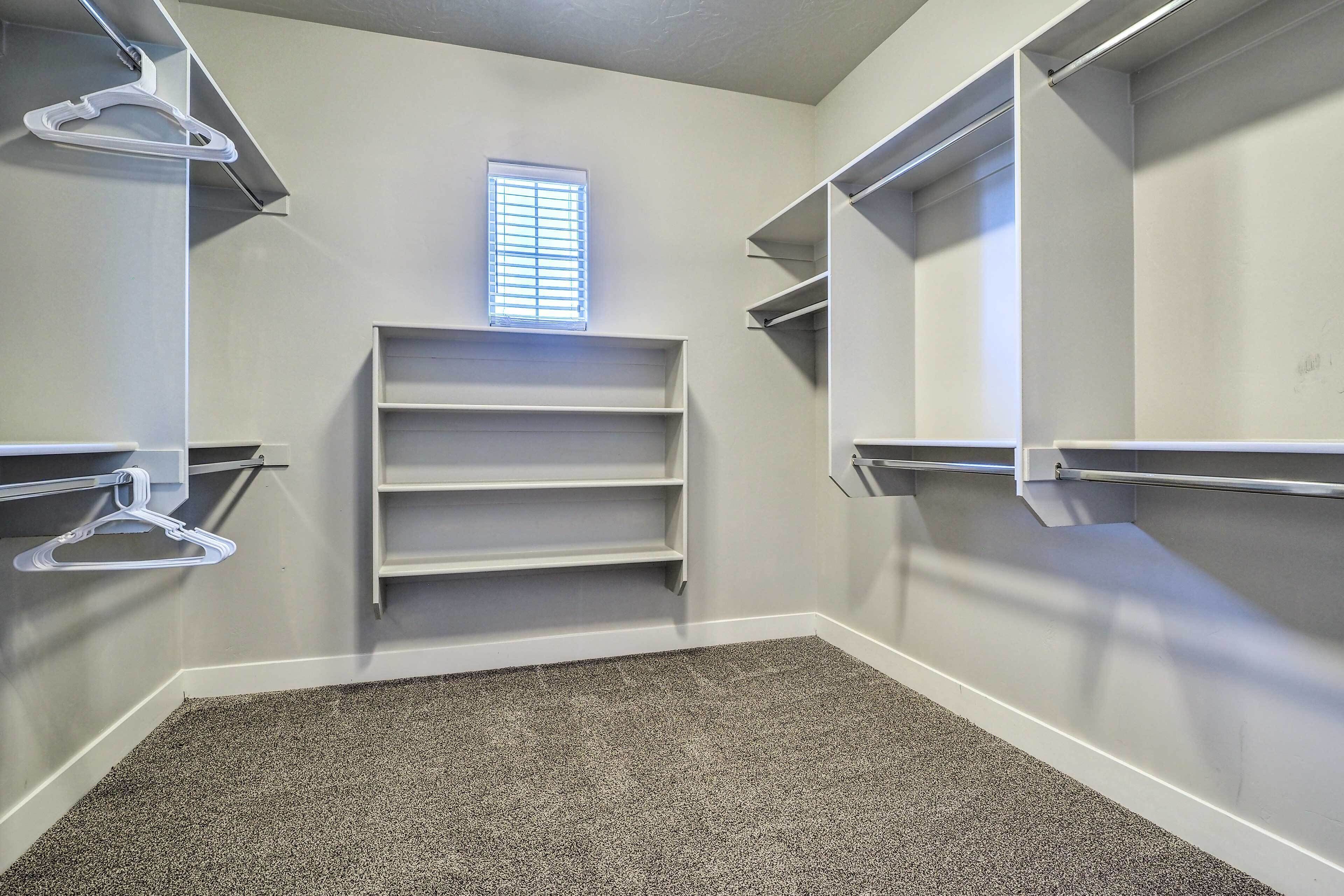 A walk-in closet with built-in shelves and a hanging rod, carpeted floor, and a window with blinds.