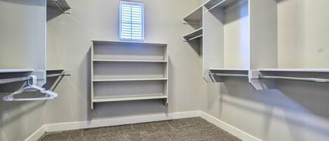 A walk-in closet with built-in shelves and a hanging rod, carpeted floor, and a window with blinds.