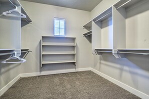 A walk-in closet with built-in shelves and a hanging rod, carpeted floor, and a window with blinds.